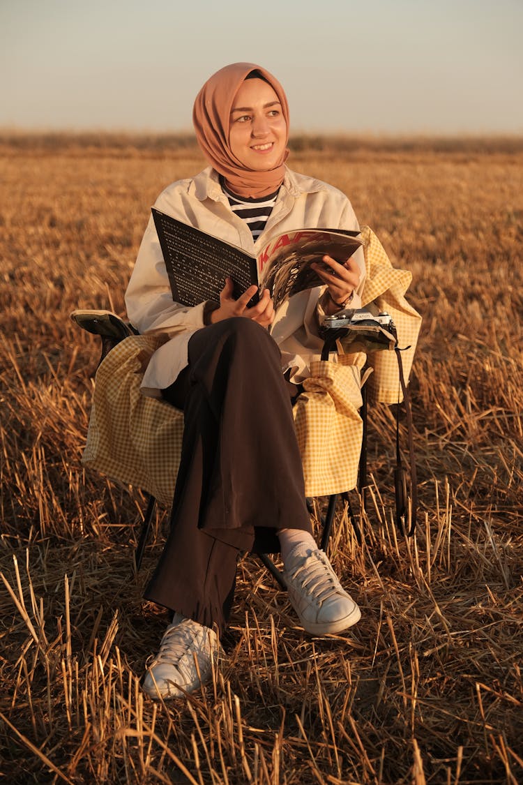 Smiling Woman In Hijab Sitting On Field At Sunset