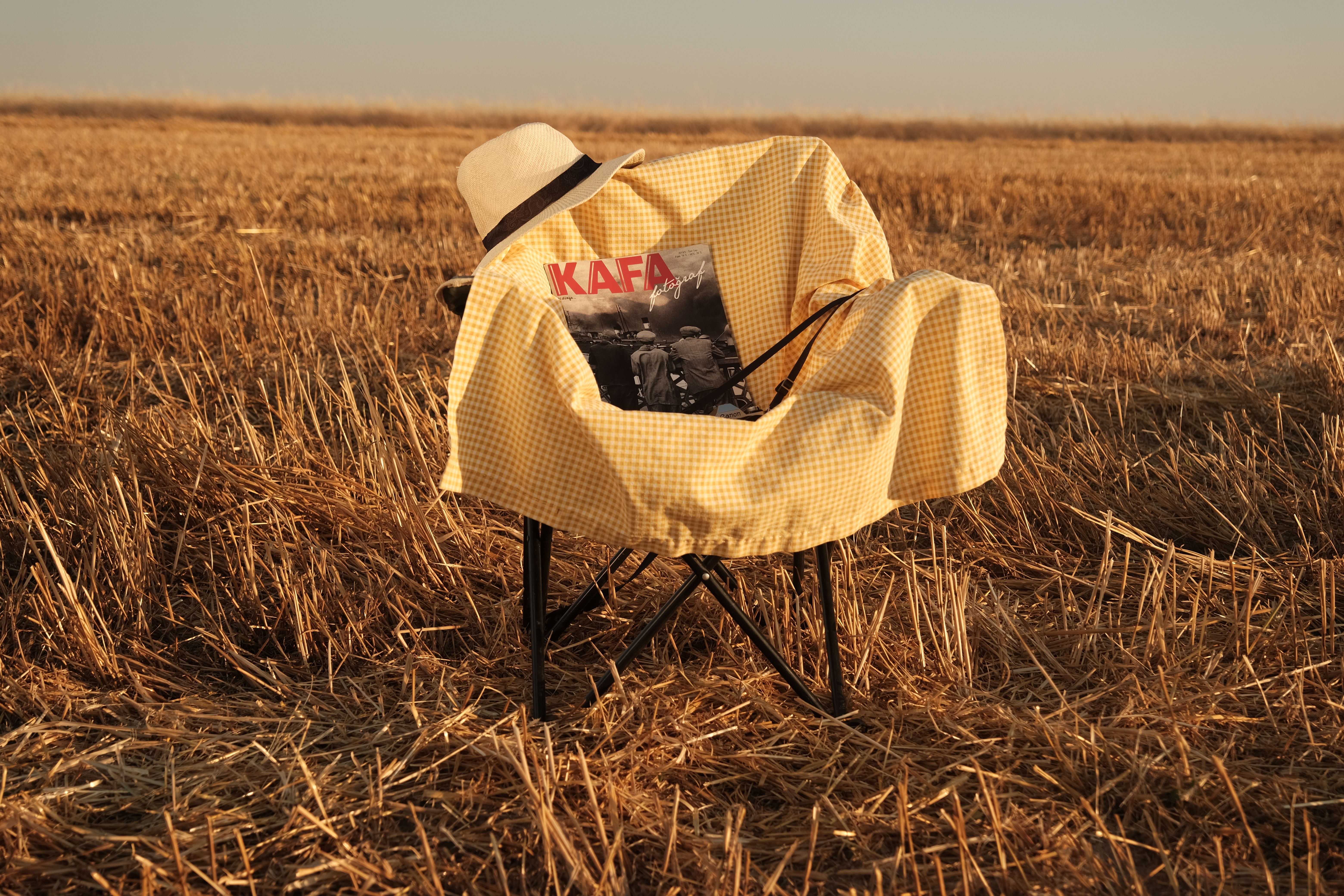 A yellow-checkered chair with a hat and magazine in a serene rural field setting.