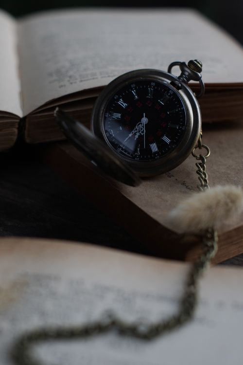 Free Classic pocket watch with chain on open books, showcasing timeless elegance and historical charm. Stock Photo