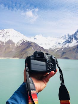 Hand holding a camera in front of snow-capped mountains and lake in Chile's Las Yeseras.