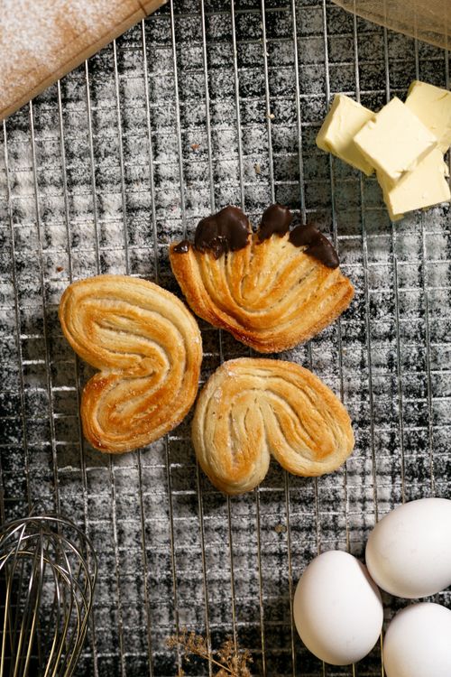 Free Top view of heart-shaped pastries on a cooling rack with eggs and butter. Stock Photo