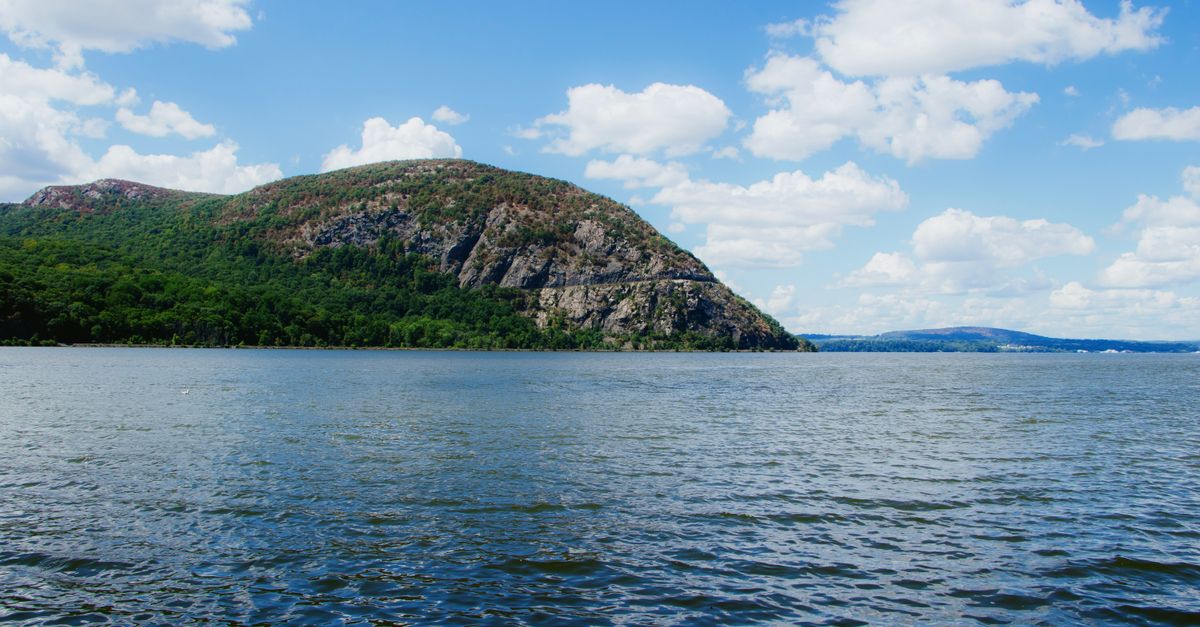 Beautiful landscape of Bear Mountain reflected in the Hudson River under a clear blue sky.