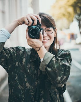 A smiling woman in glasses takes a photo outdoors, capturing a moment.