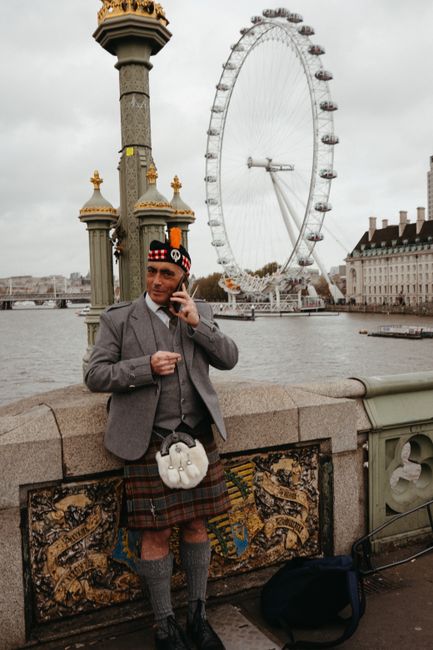 A man in traditional Scottish attire stands by the London Eye, capturing urban culture.