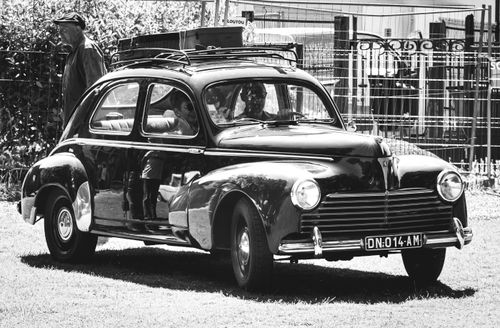 Free Black and white photo of a vintage Peugeot car with whitewall tires, captured in an urban setting. Stock Photo