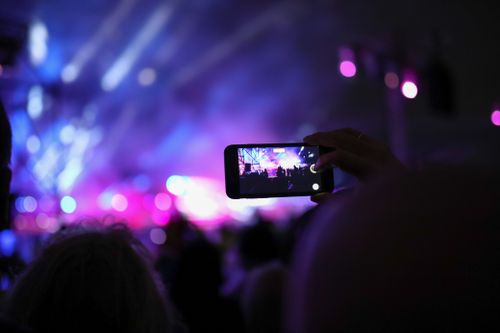 Free A vibrant nighttime concert captured with dynamic lights and a smartphone in focus. Stock Photo