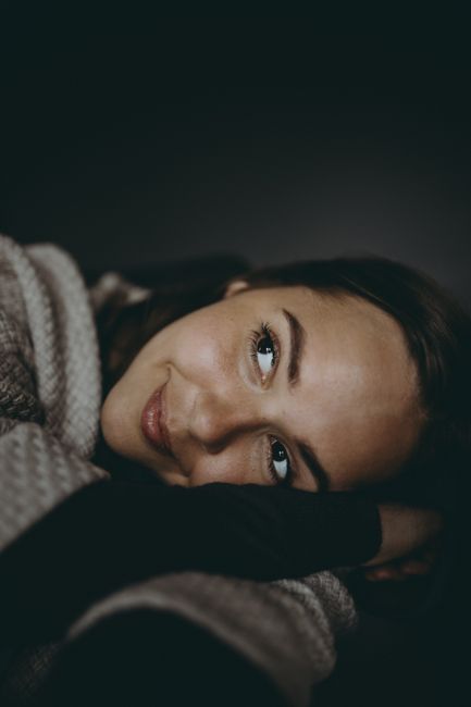 Close-up portrait of a smiling woman in cozy sweater against a dark background, conveying warmth and comfort.