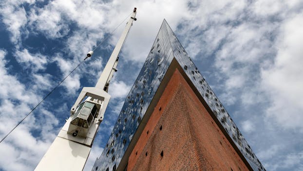 Upward view of Hamburg's Elbphilharmonie and nearby crane under a blue sky with clouds.