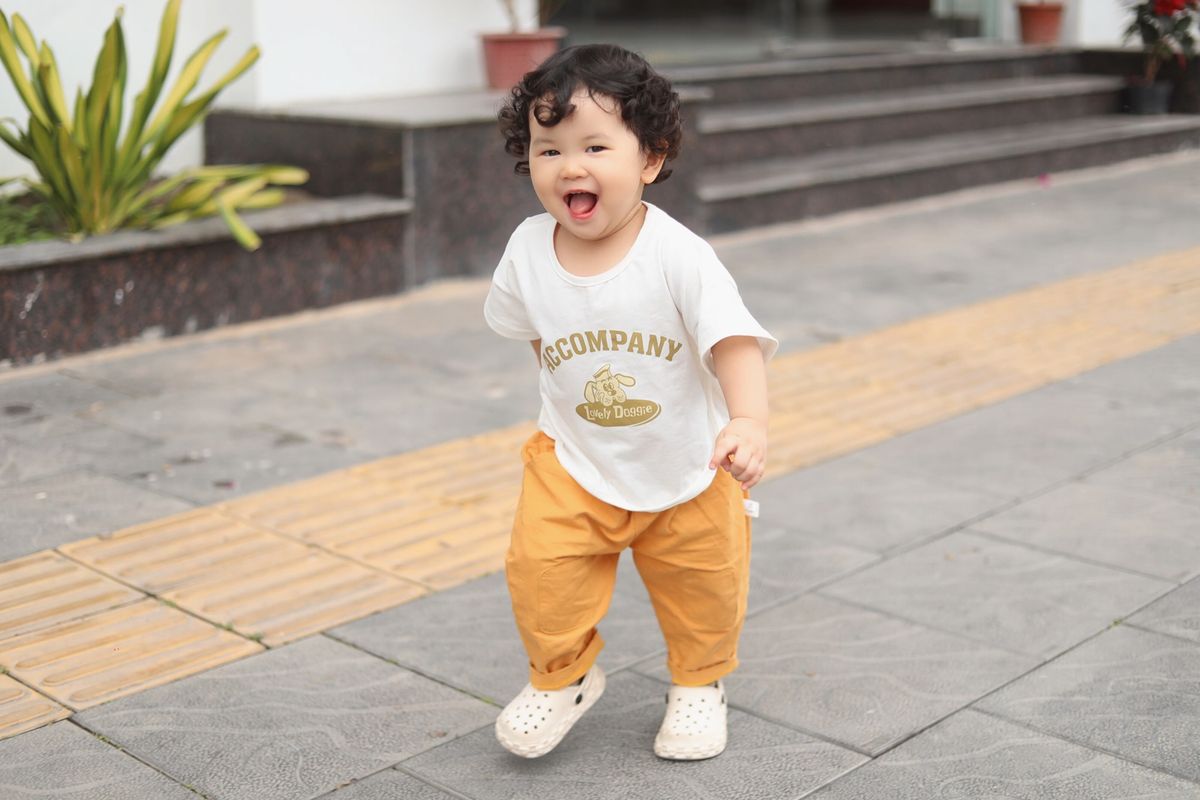 A cute baby walking on a pavement and smiling