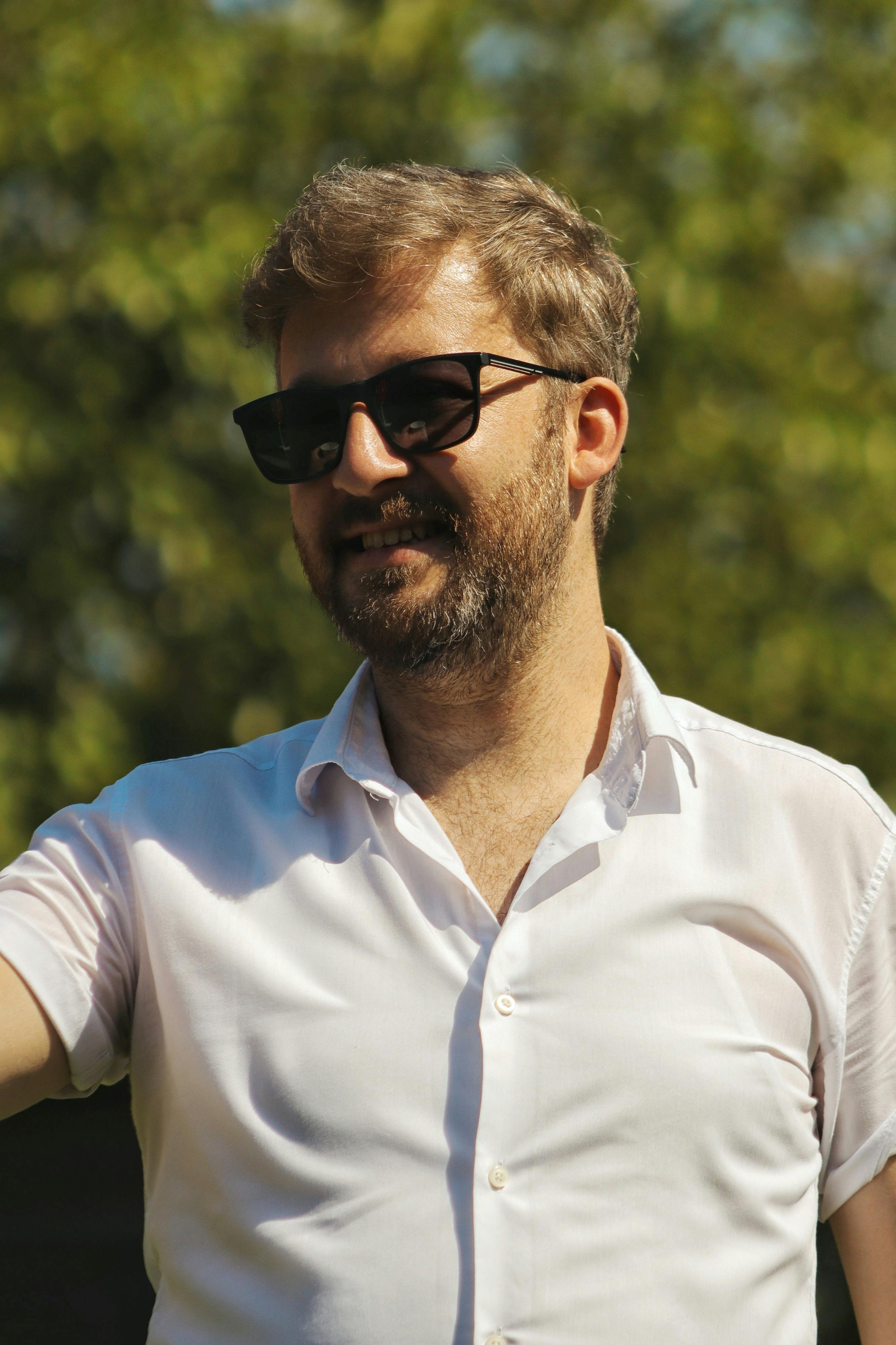 Portrait of a man wearing sunglasses and a white shirt enjoying a sunlit day outdoors.