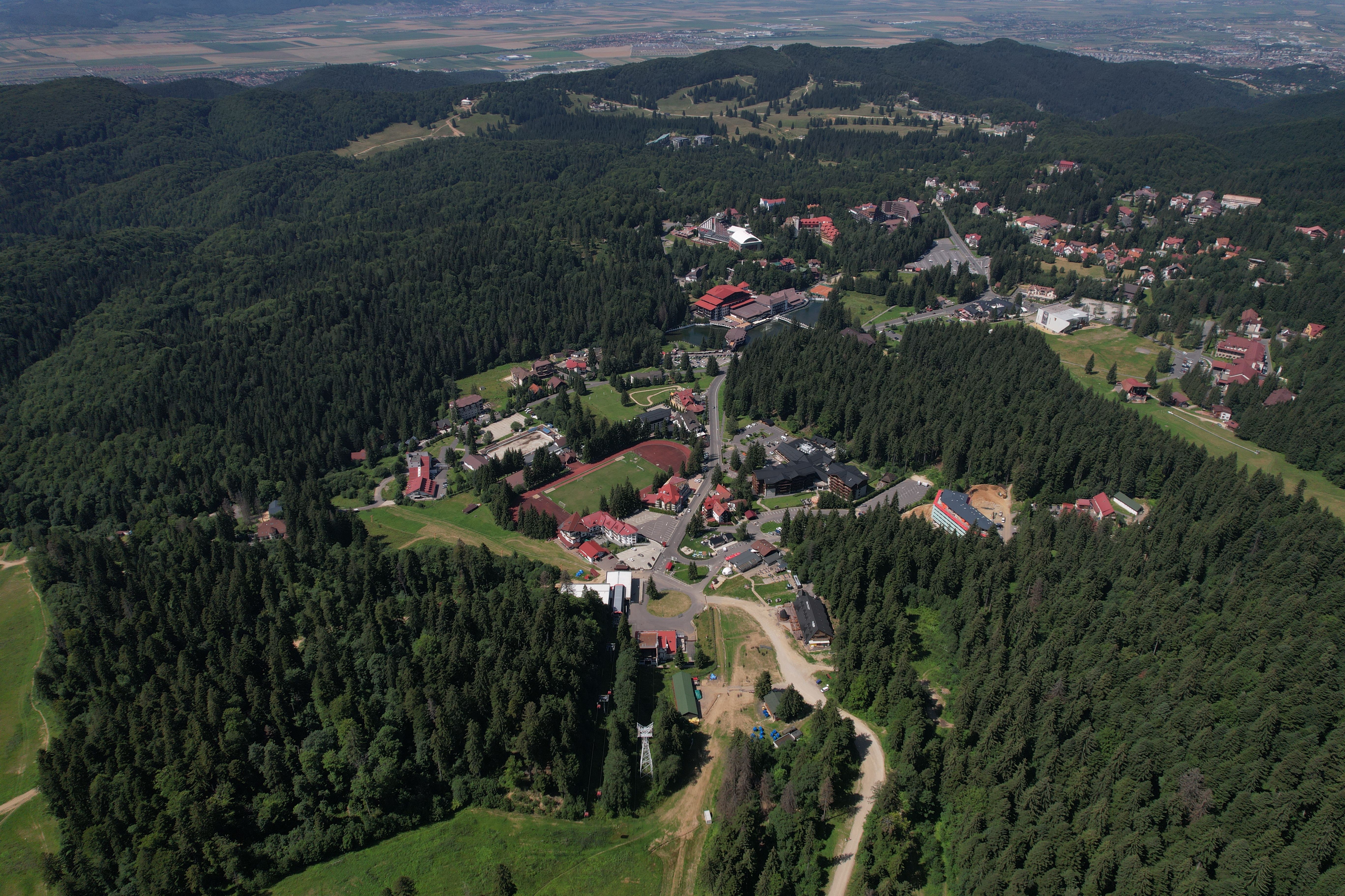 Drone view of a forested town nestled in lush green hills with distant landscapes.