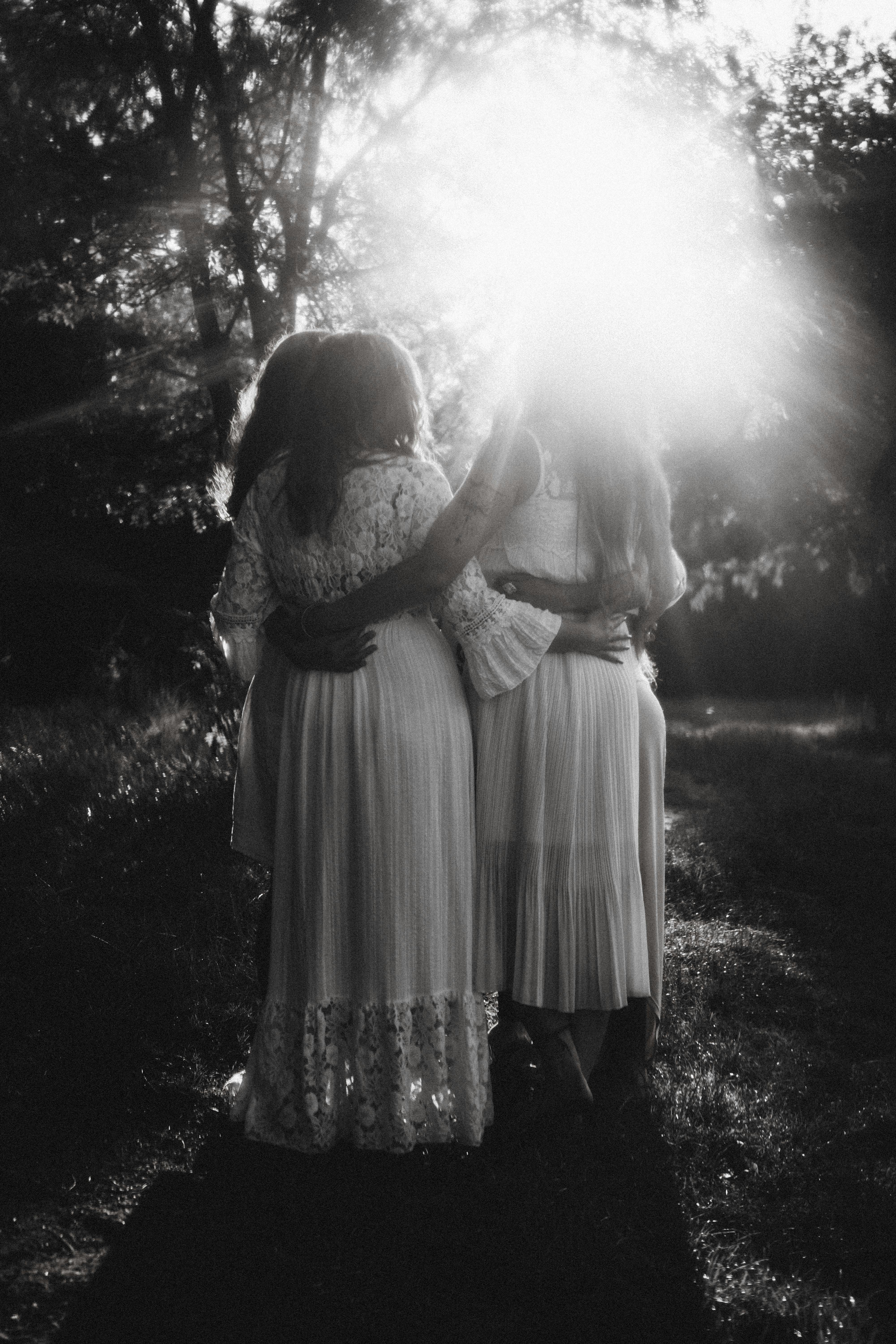 Black and white image of women hugging in a sunlit meadow, evoking serenity.