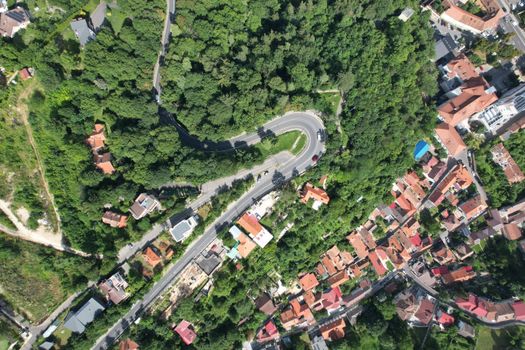 Overhead view of a sunny urban neighborhood with winding roads and lush greenery.