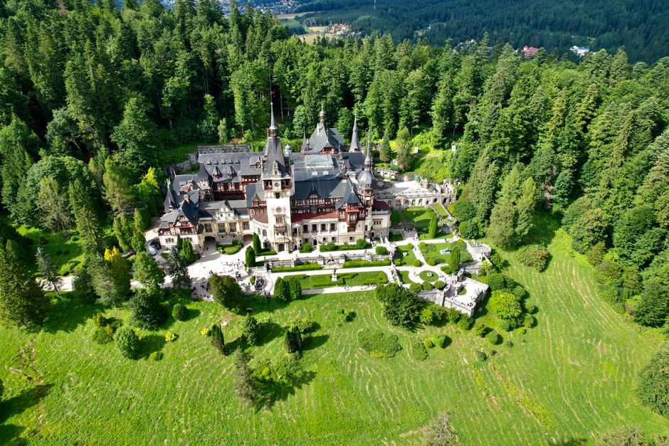 Majestic Peles Castle surrounded by verdant forest in Romania, viewed from above.