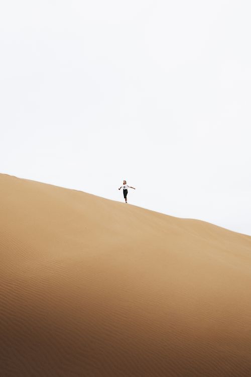 Free Silhouetted woman running on vast sand dunes under a bright sky in Antalya, Turkey. Stock Photo