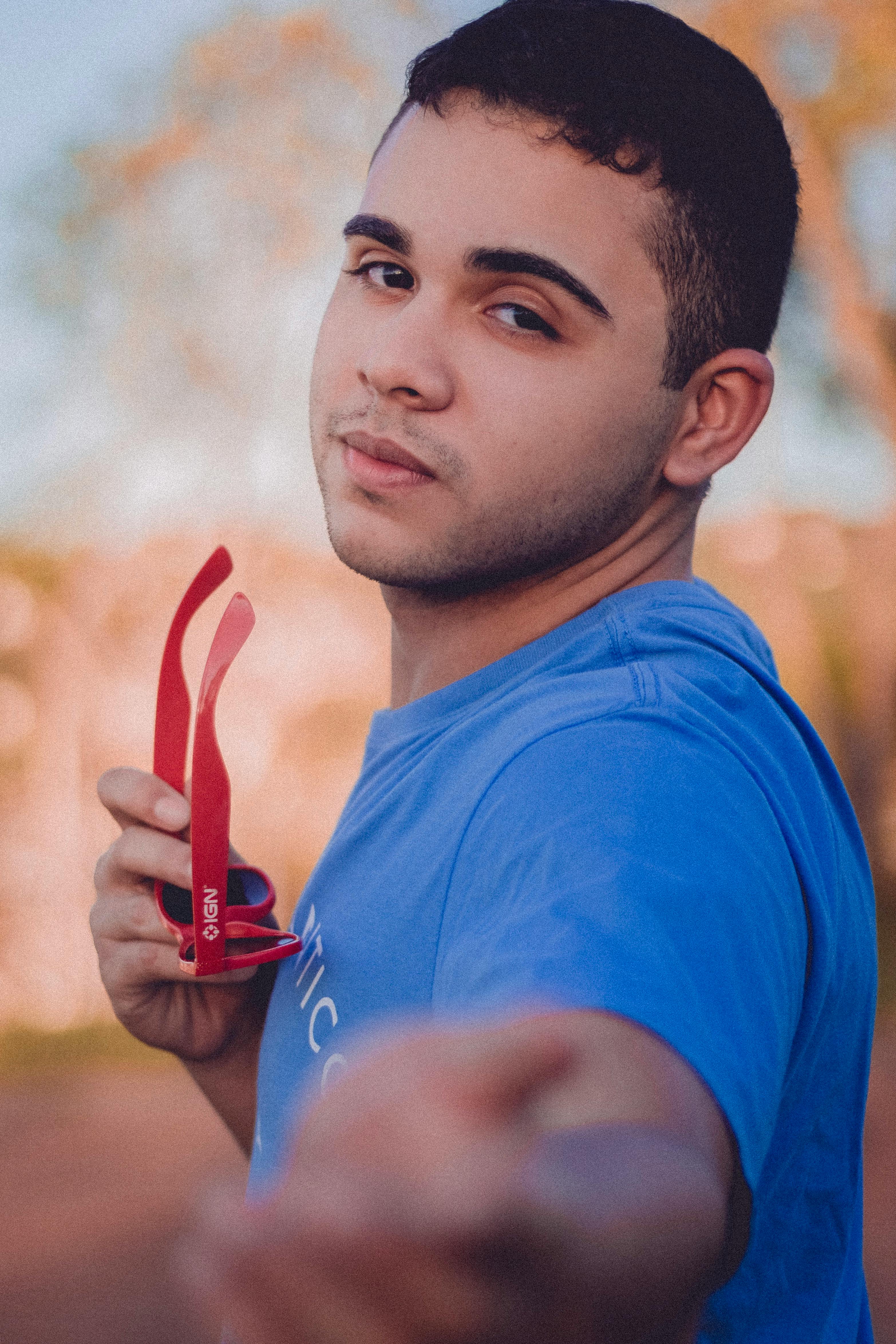 一名年轻男子在户外手持红色太阳镜，色调温暖