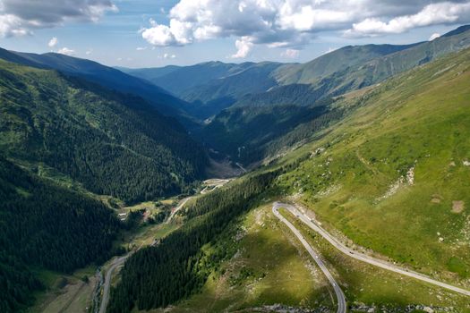 Stunning aerial shot capturing the lush green mountain valley with winding roads and dense forests.