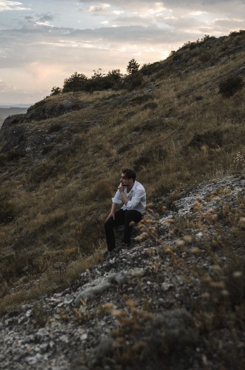 Free A thoughtful man sitting on a rocky hill, enjoying the serene sunset view. Stock Photo