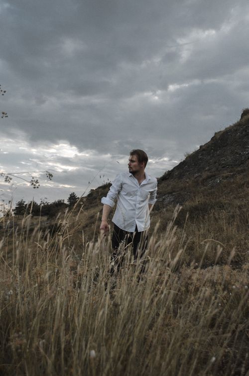 Free A man in a field of tall grass under cloudy skies, showcasing a serene and natural landscape. Stock Photo