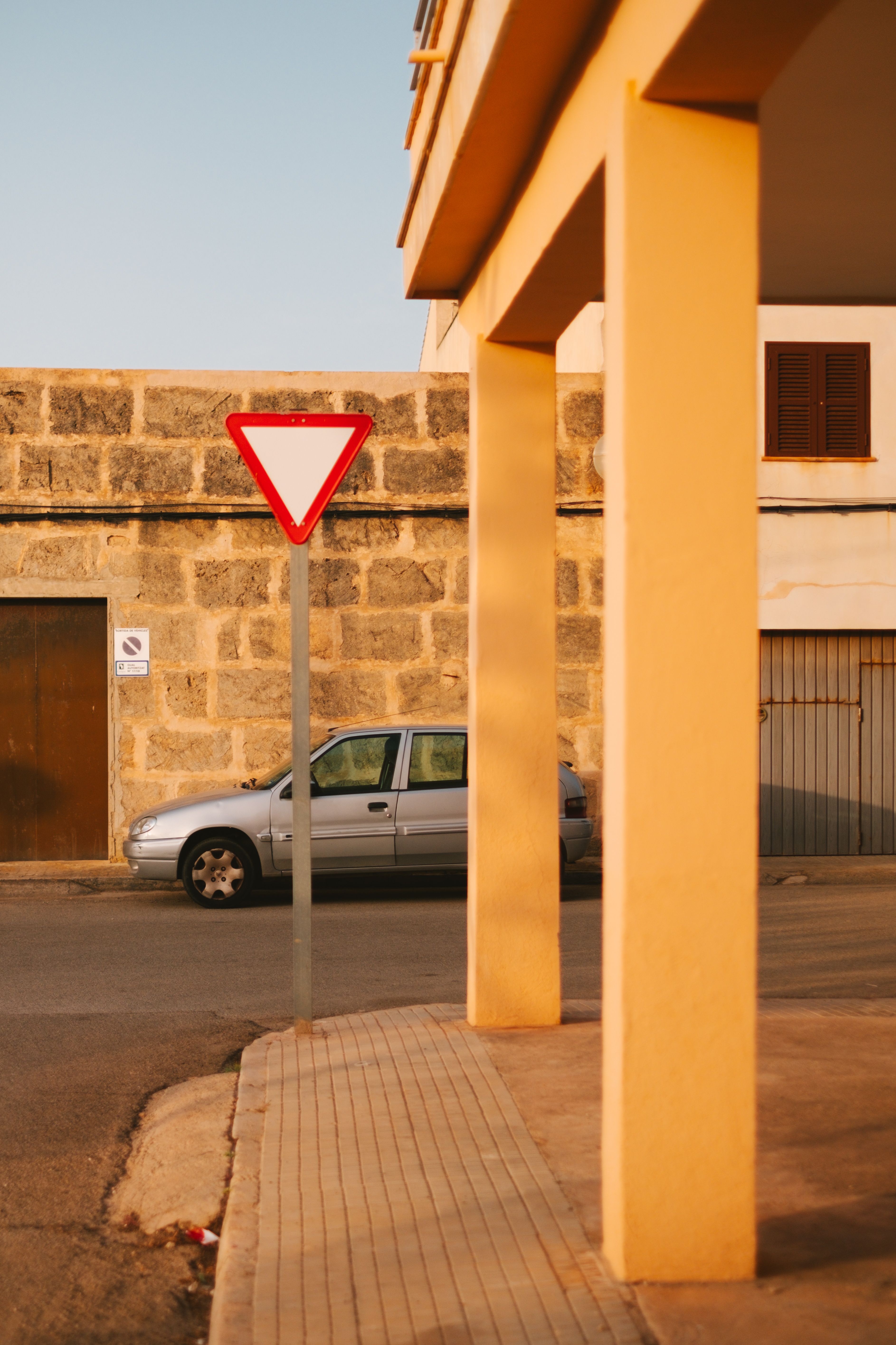 Street view featuring a parked car and a yield sign in the warm summer streets of Sa Ràpita, Spain.