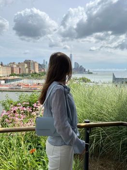 A woman stands by railing, overlooking the iconic New York City skyline and the Hudson River.