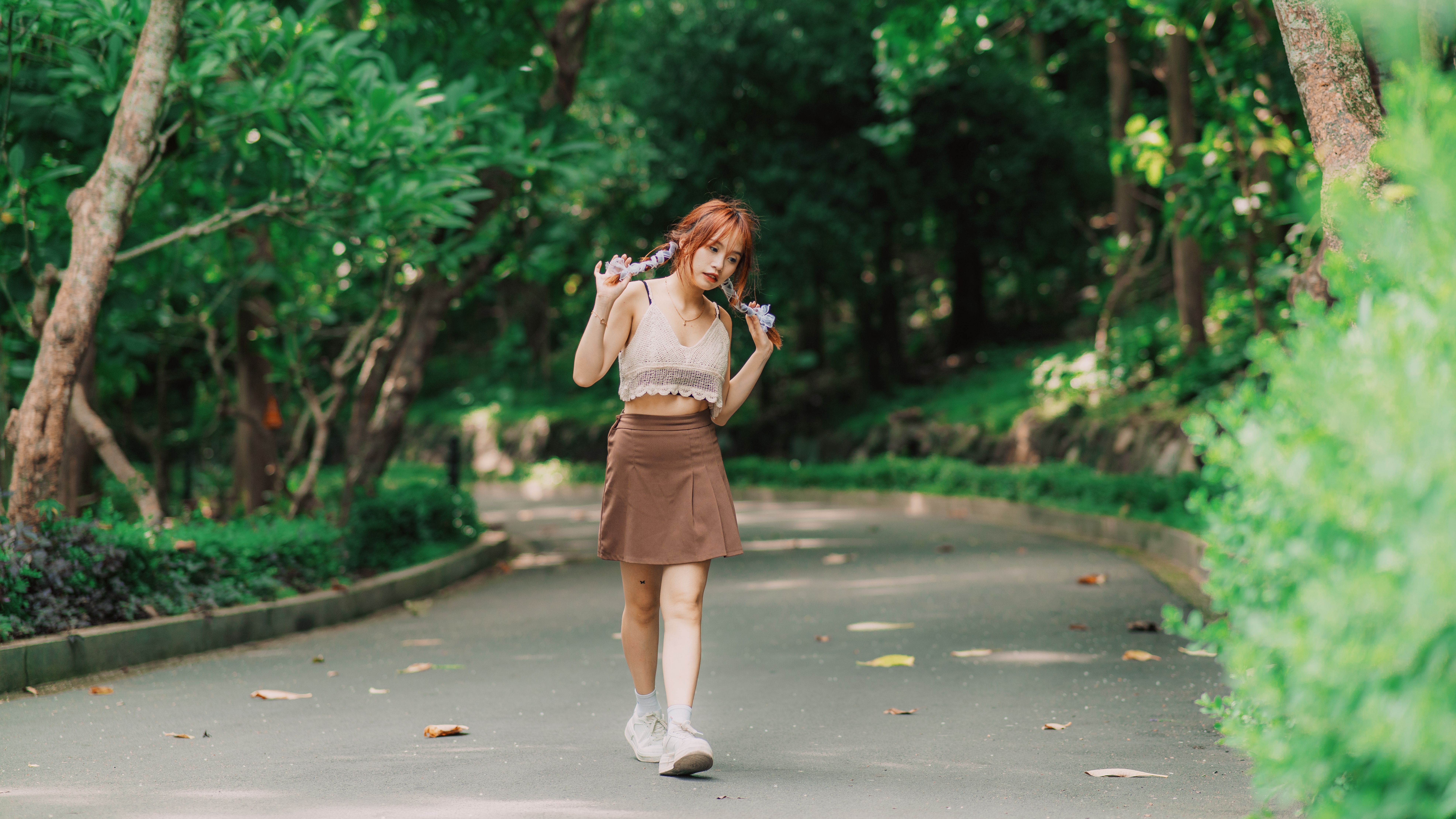 Asian woman in white top and brown skirt walking in a lush park in Vung Tau, Vietnam.