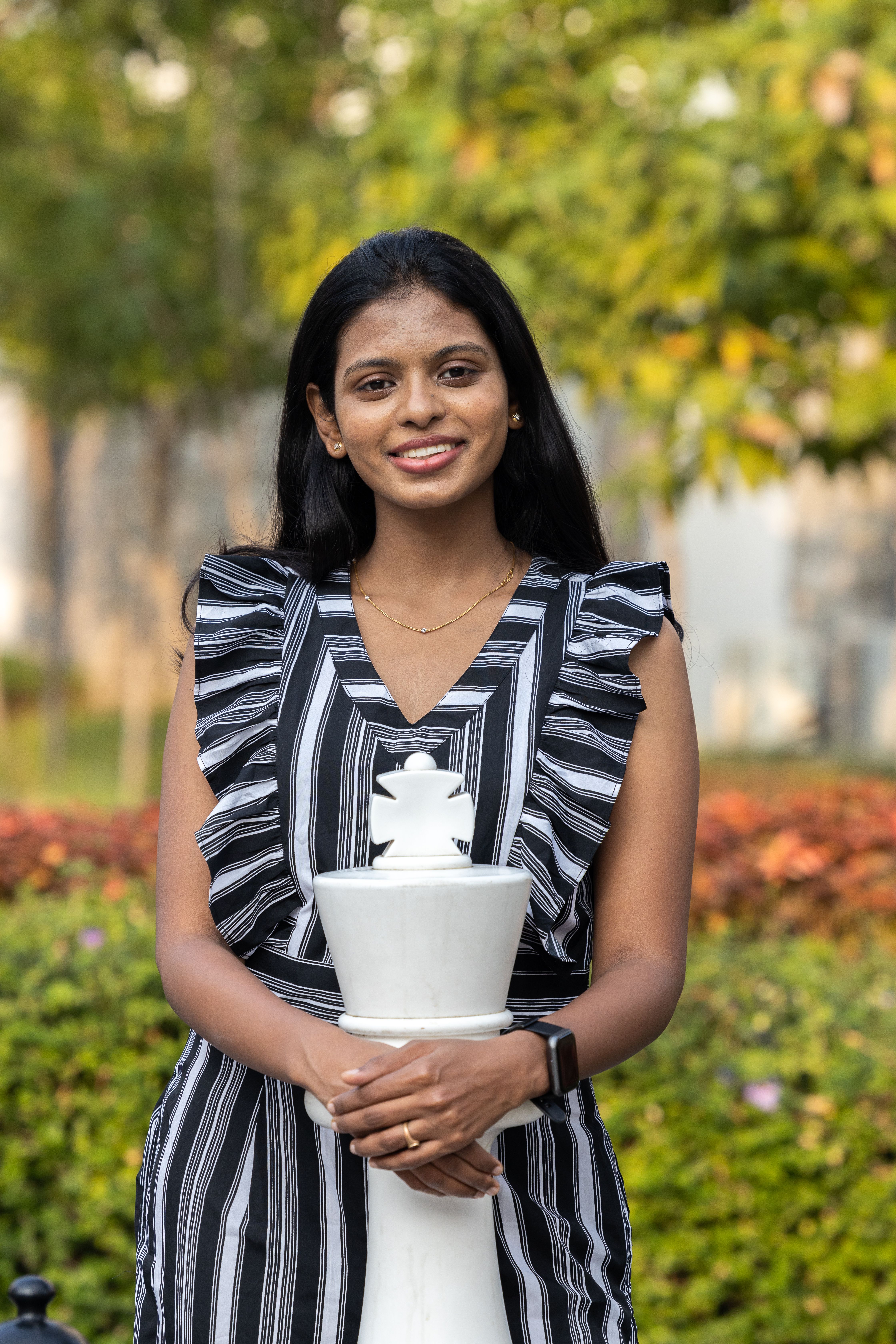 Smiling woman in a striped dress posing with a large chess piece in Hyderabad, India.