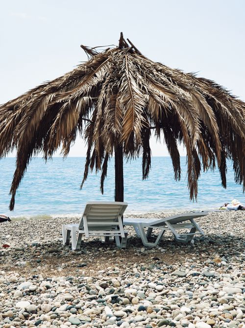 Free Peaceful beach with palm umbrella and deckchairs by the sea. Stock Photo