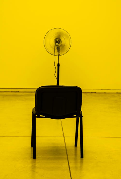 Free Turned-on Black Pedestal Fan Facing Empty Chair Stock Photo