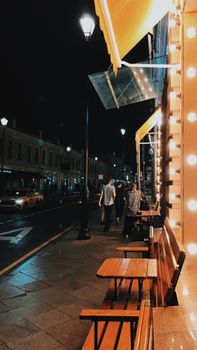 Nighttime urban street view in Moscow with illuminated restaurant facade and people walking.