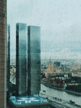 A rainy view of Moscow's cityscape featuring modern skyscrapers and the Moskva River.