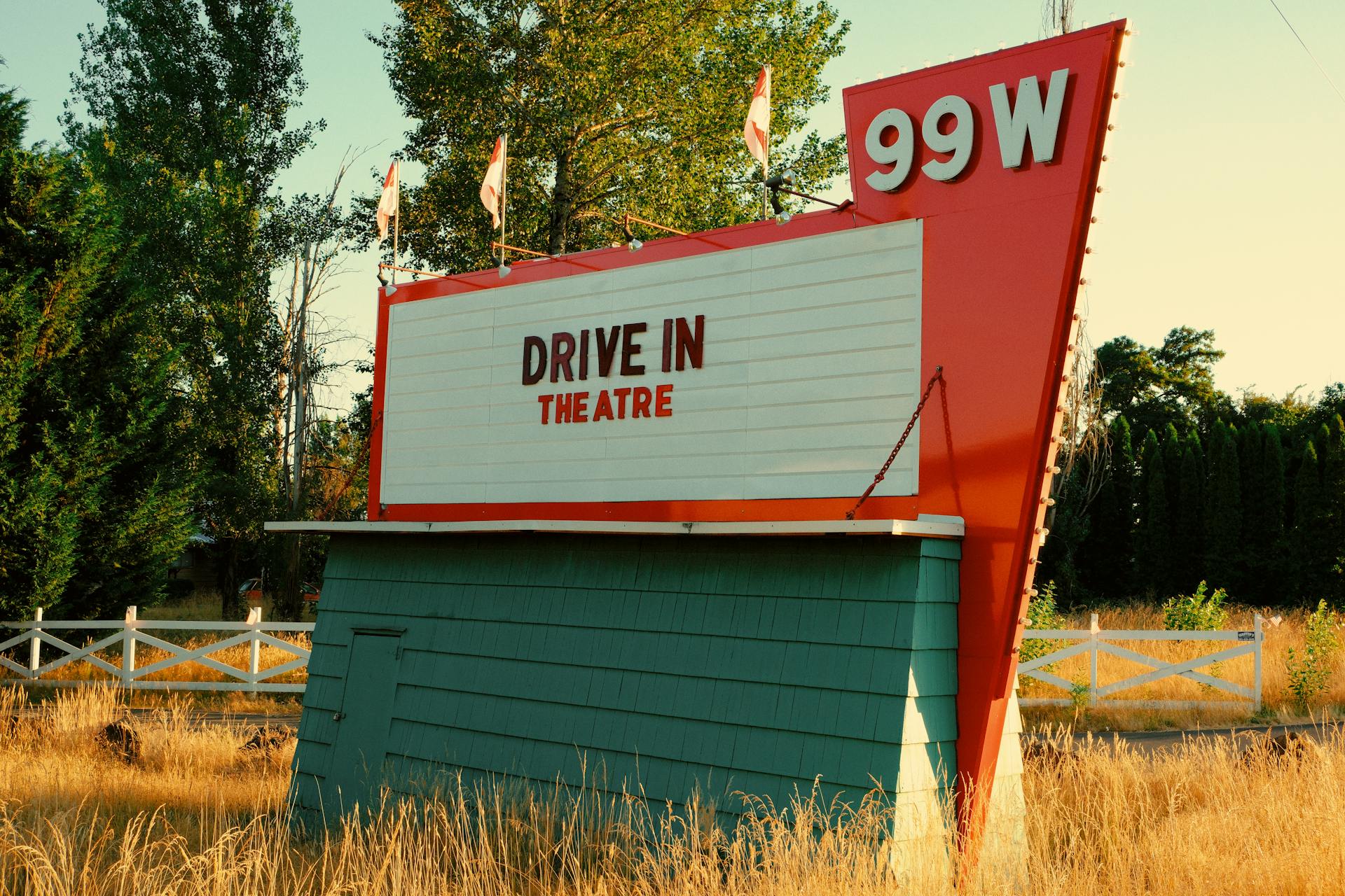 Vintage drive-in theatre sign in the countryside surrounded by trees and grasses.