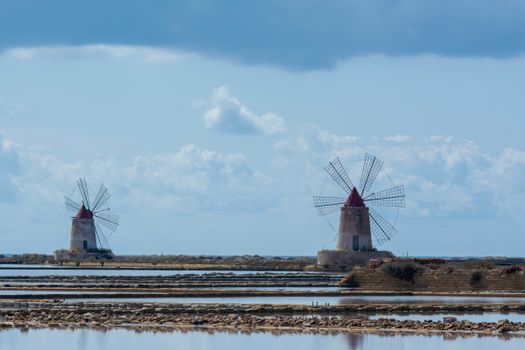 Scenic view of traditional windmills at Nubia's salt flats in Sicily, Italy under a cloudy sky.