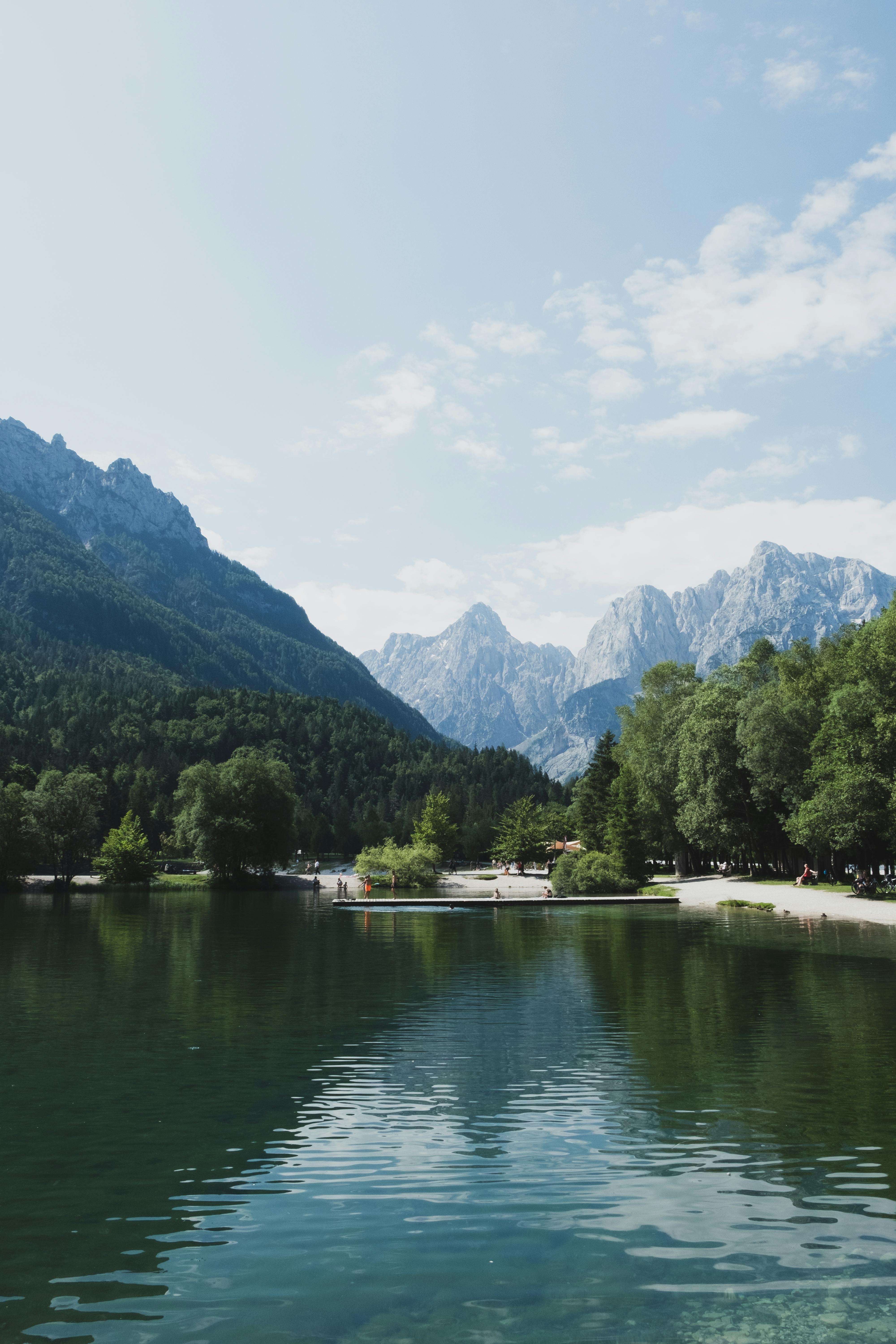Serene mountain lake scene with lush forest and majestic peaks on a calm day.