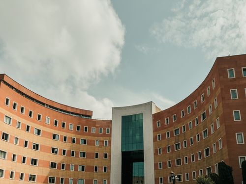Free A modern curved building with red brick facade and windows under a cloudy sky, showcasing urban architecture. Stock Photo