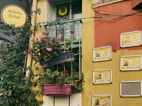 Charming facade with balcony flowers and real estate signs on a colorful building.