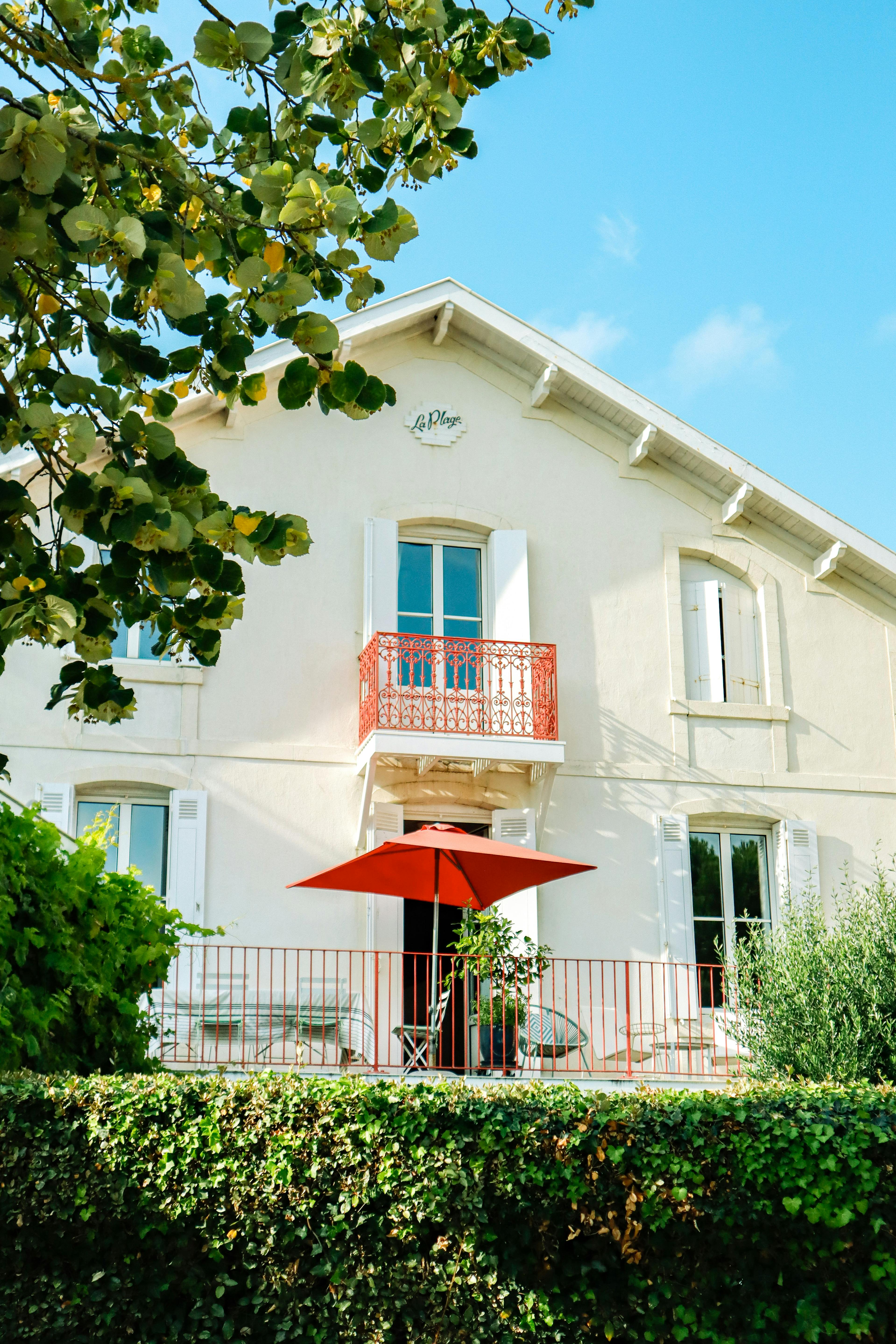 Elegant rural house featuring a red sunshade and balcony, surrounded by greenery.