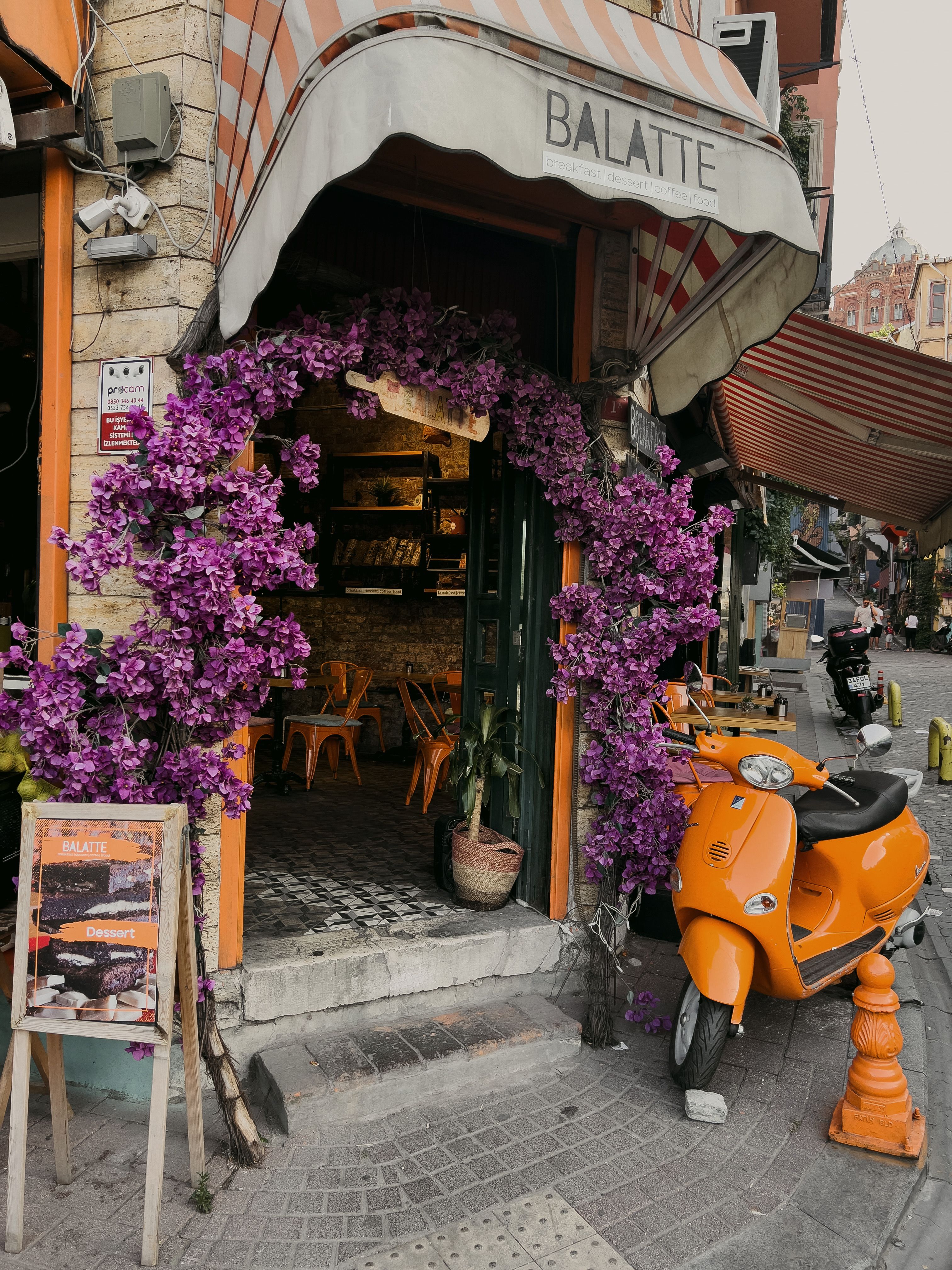 Cozy café entrance in Istanbul adorned with vivid purple flowers and a vibrant scooter parked outside.