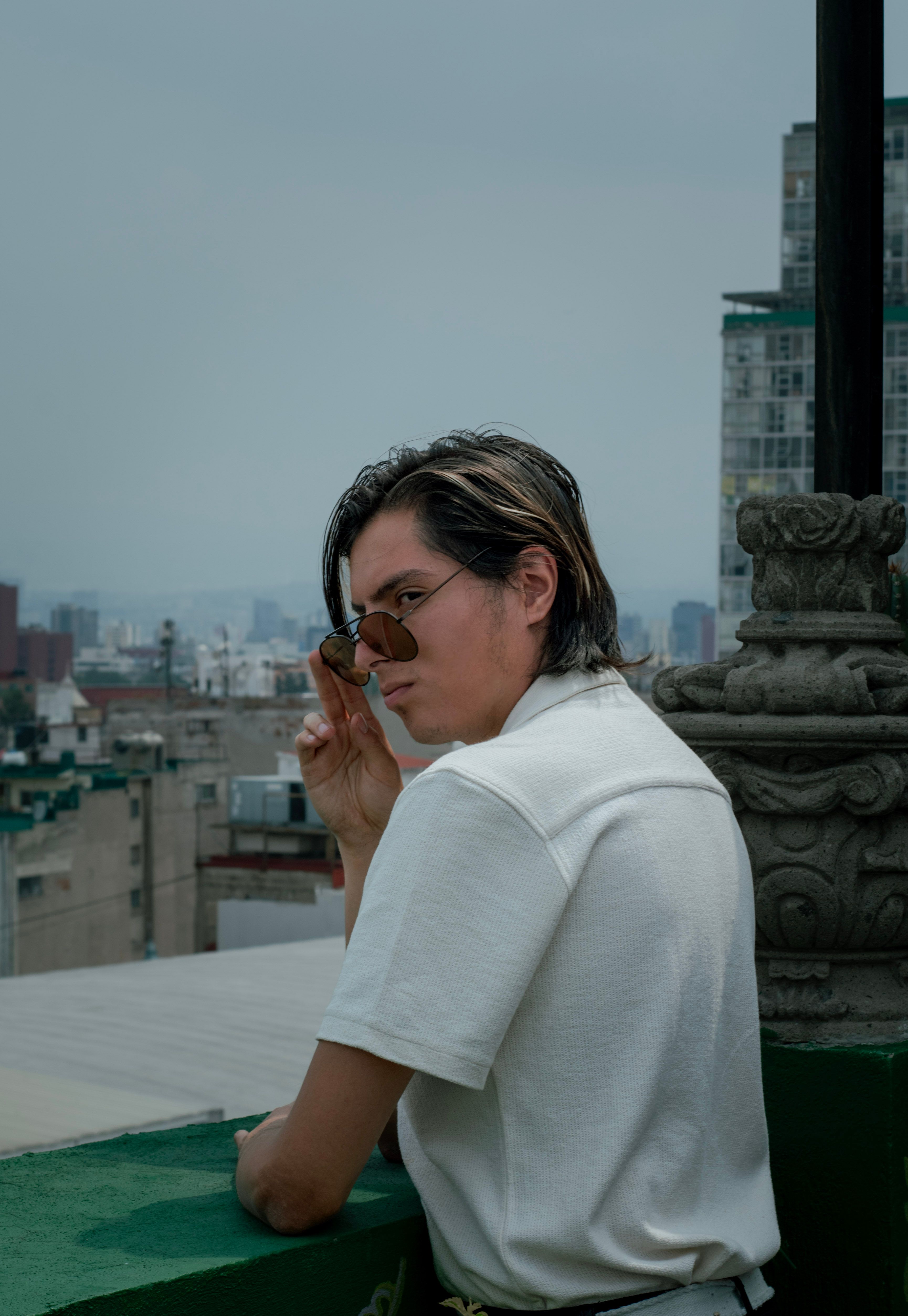 Portrait of a man wearing sunglasses on a rooftop, overlooking Mexico City's urban skyline.