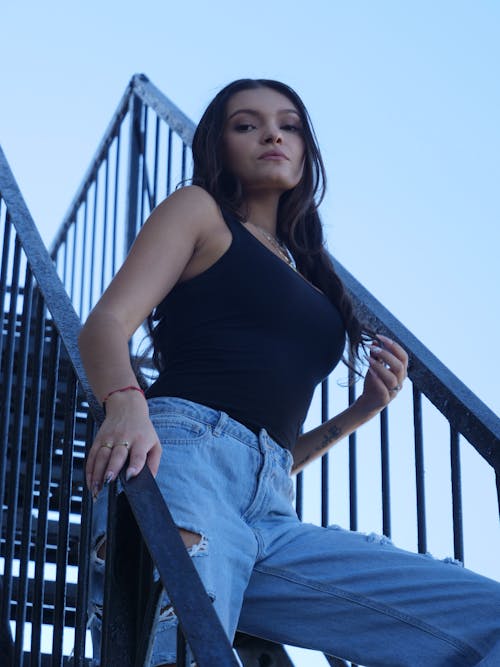 Model in a Black Tank Top and Distressed Jeans Standing on the Stairs