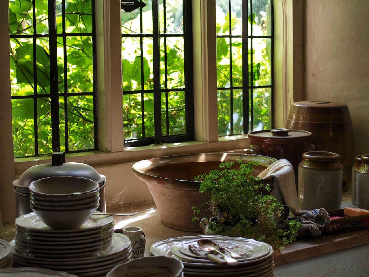 Stoneware crocks and stacked dishes on a farmhouse counter beside a leaded glass window