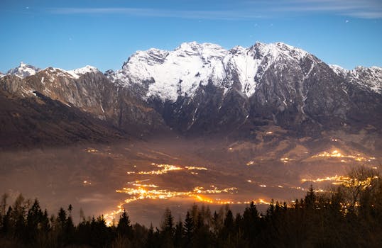 Breathtaking view of a snow-capped mountain range with city lights glowing in the valley below.