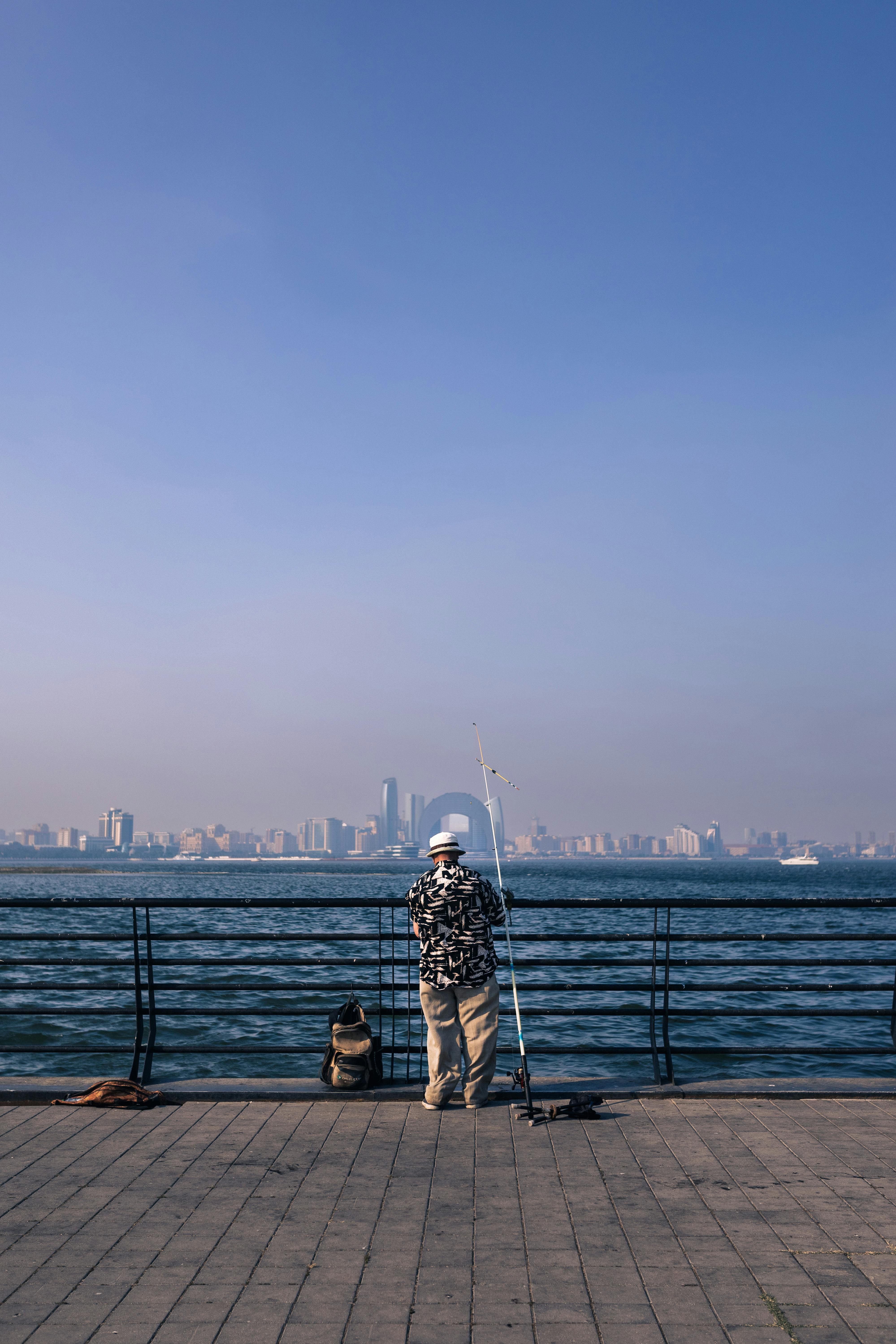 A man fishing on a promenade with a clear view of Baku's skyline across the sea.