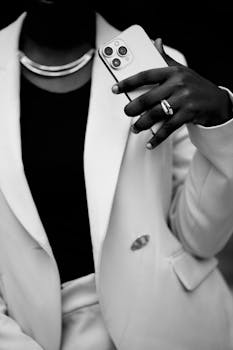 Black and white photo of a person in a suit holding a smartphone, exuding style and confidence.