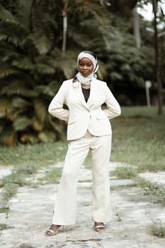 Young businesswoman in a white suit posing confidently at a park, showcasing elegance and style.