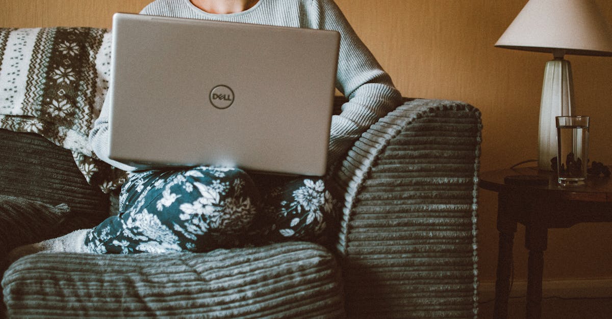 Uma mulher vestindo roupas casuais trabalha em um laptop enquanto relaxa em um sofá aconchegante dentro de casa.