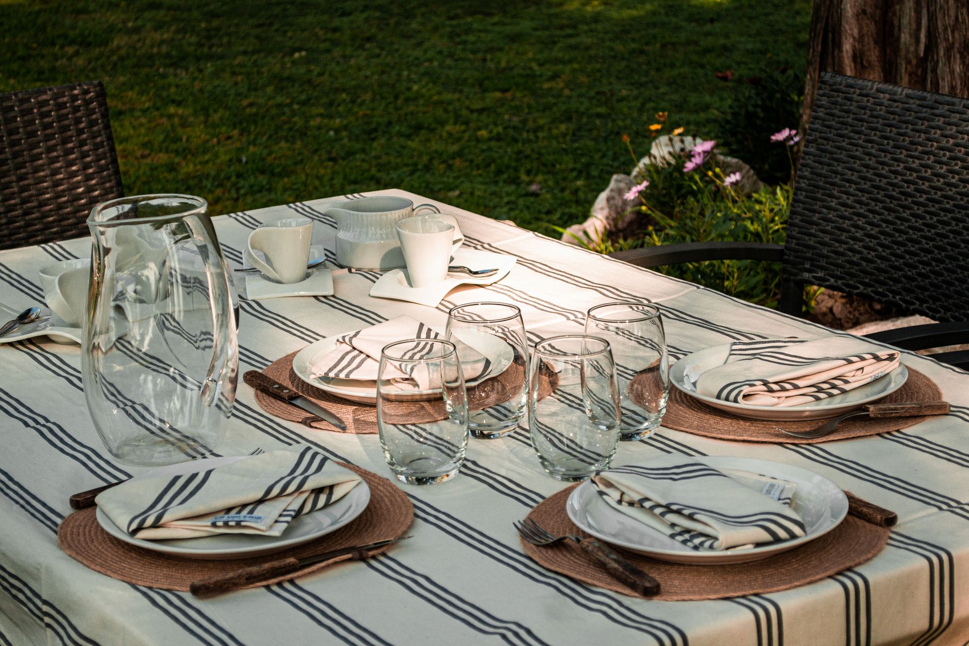 An elegant outdoor table setup with cutlery, glassware, and striped tablecloth for casual dining.