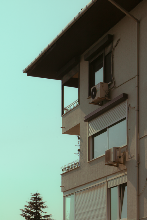 Free Close-up of a modern apartment building with visible air conditioners and balconies under a clear sky. Stock Photo