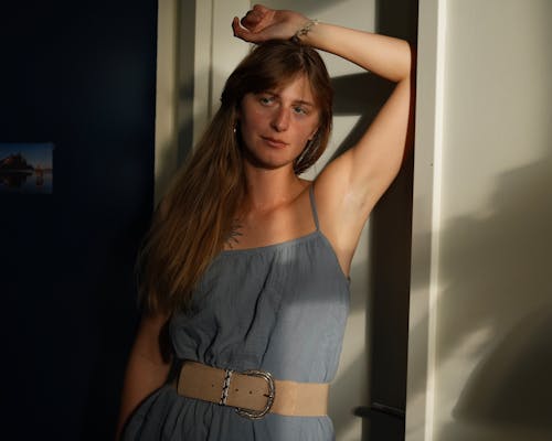 A woman in a blue dress leaning against a door