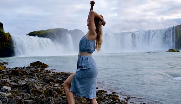 Graceful woman in a blue dress dancing by the scenic Godafoss waterfall in Iceland.